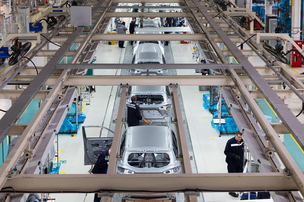 Automotive assembly line with workers installing components on partially built cars in a modern factory, representing vehicle manufacturing and supply chain operations.