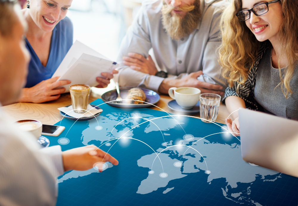 Business team reviewing global logistics strategy at a coffee table with a digital world map overlay illustrating international supply routes.