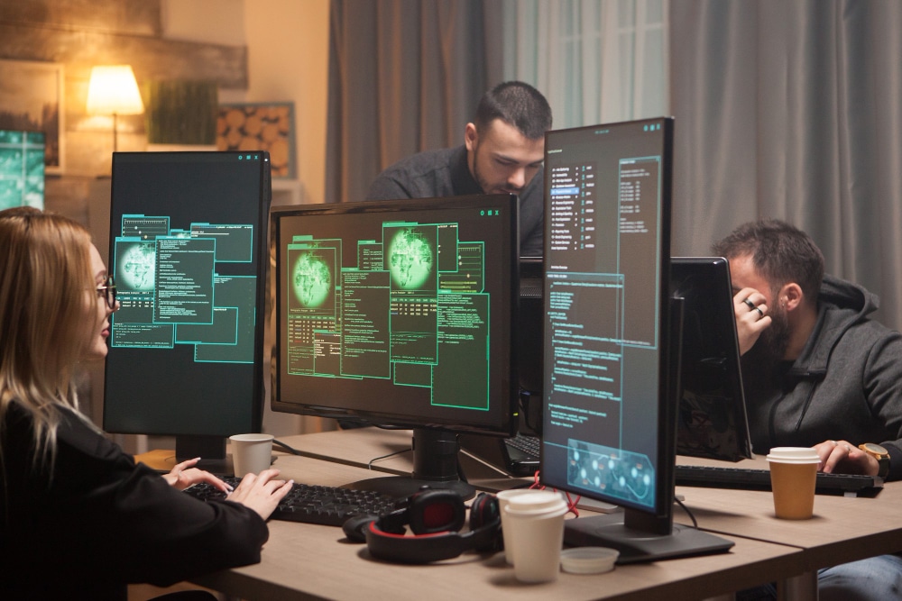 Team of cybersecurity professionals monitoring global network threats on multiple computer screens during a live supply chain risk analysis operation.